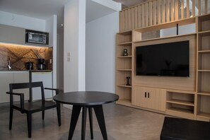 Ein modernes Wohnzimmer mit Küchenzeile, einem Esstisch und einem großen Flachbildfernseher, der an einer Holzwand angebracht ist.