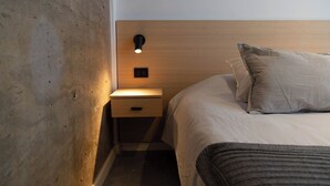 Habitació d'hotel amb un panell de capçalera de fusta, una taula de nit amb una làmpada, un llit amb coixí a ratlles i una manta fosca.
