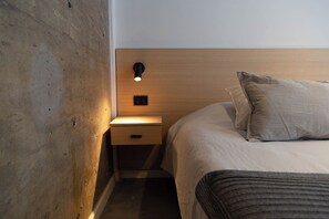 Ein Hotelzimmer mit einem hölzernen Kopfende, einem Nachttisch mit Lampe, einem Bett mit gestreiftem Kopfkissen und einer dunkel gefärbten Tagesdecke.