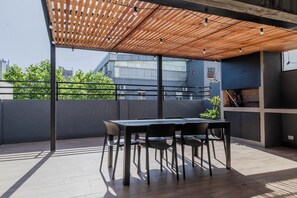 An outdoor patio with a wooden pergola, a table with chairs, and a view of buildings in the background. - Modern Recoleta Studio with BBQ Terrace and Coworking Space (Buenos Aires)