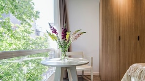 Une pièce comprenant une table ronde, une chaise, une armoire en bois et une fenêtre donnant sur un paysage verdoyant et des bâtiments.