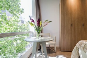 A room with a round table, a chair, a wooden wardrobe, and a window with a view of greenery and buildings. - Modern Recoleta Studio with BBQ Terrace and Coworking Space (Buenos Aires)