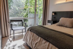 Ein Schlafzimmer mit einem Bett, einem Nachttisch, einem Stuhl und einem Fenster mit Blick auf Bäume.