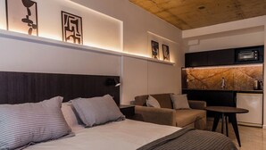 Een moderne hotelkamer met een bed, twee sofa's, een kleine tafel, een kitchenette en kunstwerken aan de wanden.