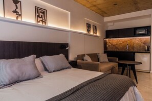 Ein modernes Hotelzimmer mit einem Bett, zwei Sofas, einem kleinen Tisch, einer Küchenzeile und Kunstwerken an den Wänden.