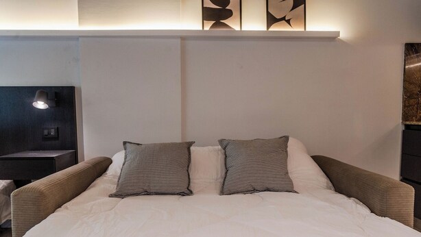 Een bed met twee kussens, een nachtkastje en een wandlamp.