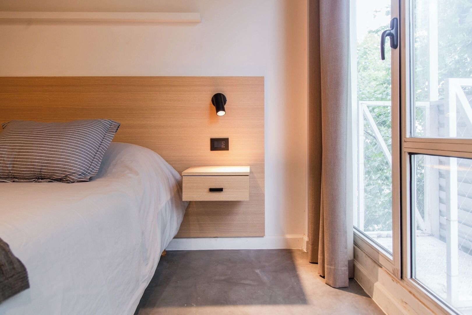 Ein Schlafzimmer mit einem Bett, einem Nachttisch mit Lampe und einem Fenster mit Vorhängen.