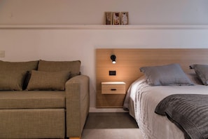 Un dormitorio con sofá, mesita de noche con lámpara y cama con almohadas a rayas.