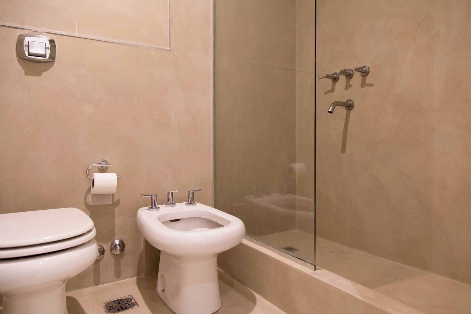 A bathroom with a toilet, bidet, and glass-enclosed shower.