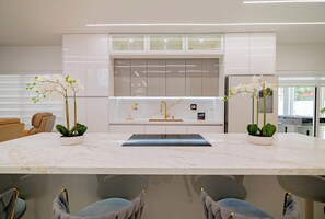 A modern kitchen with a marble countertop, two potted orchids, a built-in oven, and a refrigerator. - Nova Palm Estate, Pool, BBQ & Game Yard (Miami)