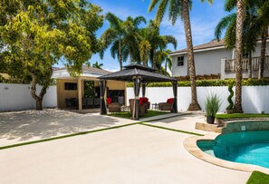 A backyard with a pool, covered patio, and outdoor seating area.