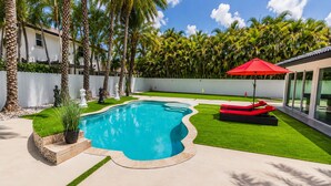 Una piscina de borde ondulado, rodeada de césped cuidado y palmeras.