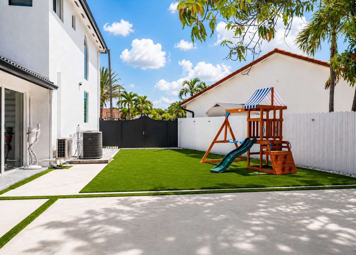A backyard with a swing set and slide, a white fence, and a building with a balcony.