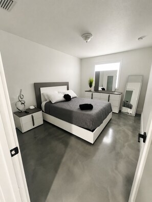Un dormitorio moderno con una cama grande, mesitas de noche, un aparador, un espejo y una lámpara en el techo.