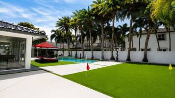 A modern house with a swimming pool, a covered patio, and a well-maintained lawn.