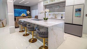 Una cocina moderna con una isla de mármol, taburetes de bar, horno empotrado y refrigerador.