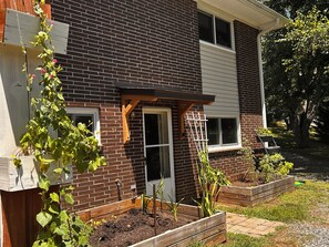 Ein Backsteinhaus mit einer Holzveranda, einem Fenster und erhöhten Blumenbeeten.
