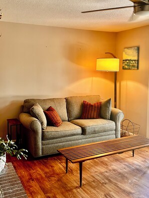 A living room with a sofa, a lamp, a painting, and a wooden floor. - Cozy 1-bedroom apartment in lovely Weaverville with AC (Weaverville)