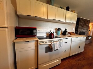 A kitchen with white cabinets, a red microwave, a stove, and a kettle. - Cozy 1-bedroom apartment in lovely Weaverville with AC (Weaverville)