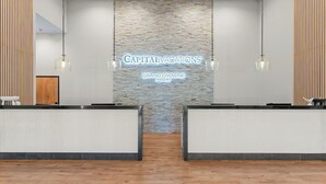 Zona de recepción con pared de piedra, dos mostradores de recepción, lámparas colgantes y un cartel que dice 'Capitalvacations Grand Crowne Resort'.