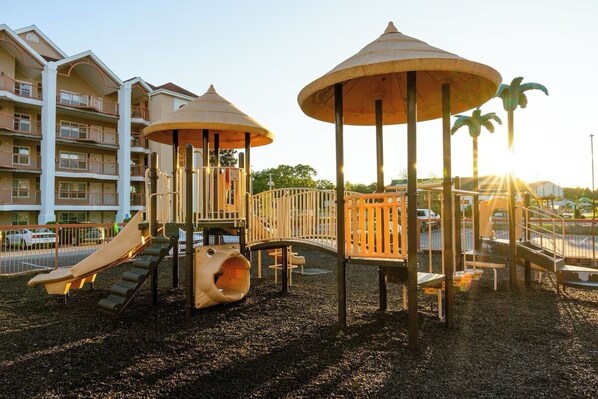 Ein Spielplatz mit Rutschen und Klettergerüsten, umgeben von einem Gebäude mit Balkonen.
