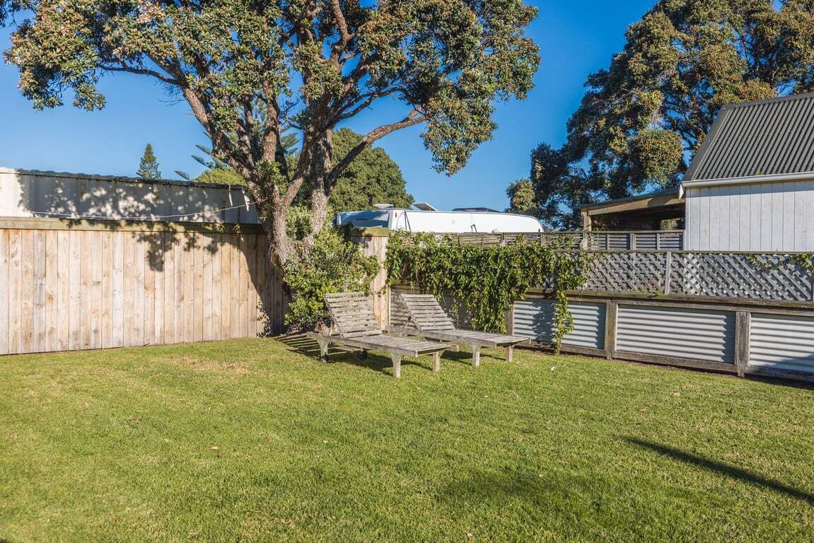 Un patio trasero con valla de madera, un árbol y una casa móvil blanca.