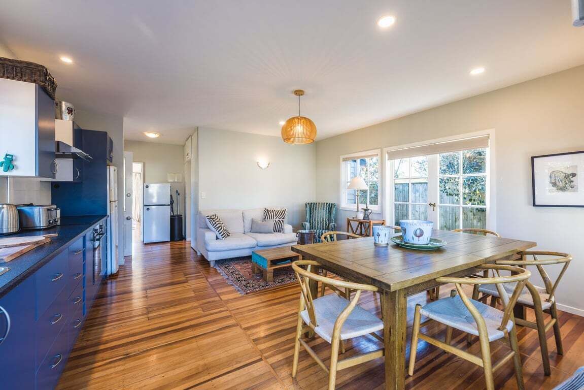 A modern kitchen with wooden flooring, a dining area with a wooden table and chairs, and a living room with a sofa and a coffee table.