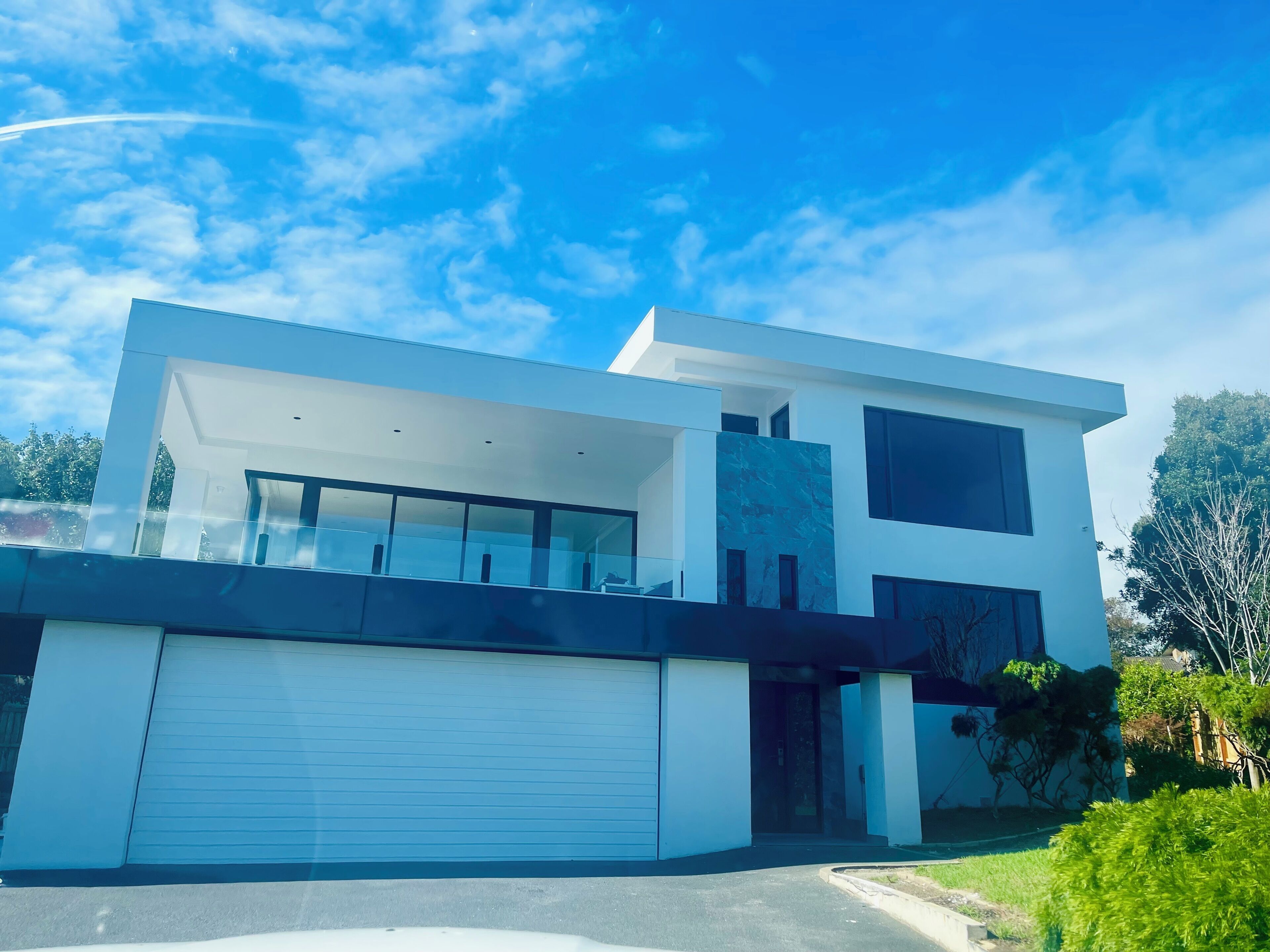 A modern two-story house with a garage, large windows, and a flat roof.