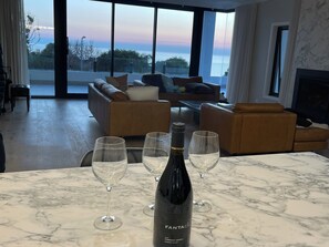 A modern living room with a large window, a fireplace, and a marble table with wine glasses and a bottle.