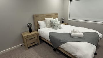 A neatly made bed with a grey throw, white pillows, and a wooden headboard. There are two bedside tables with lamps and a small drawer.