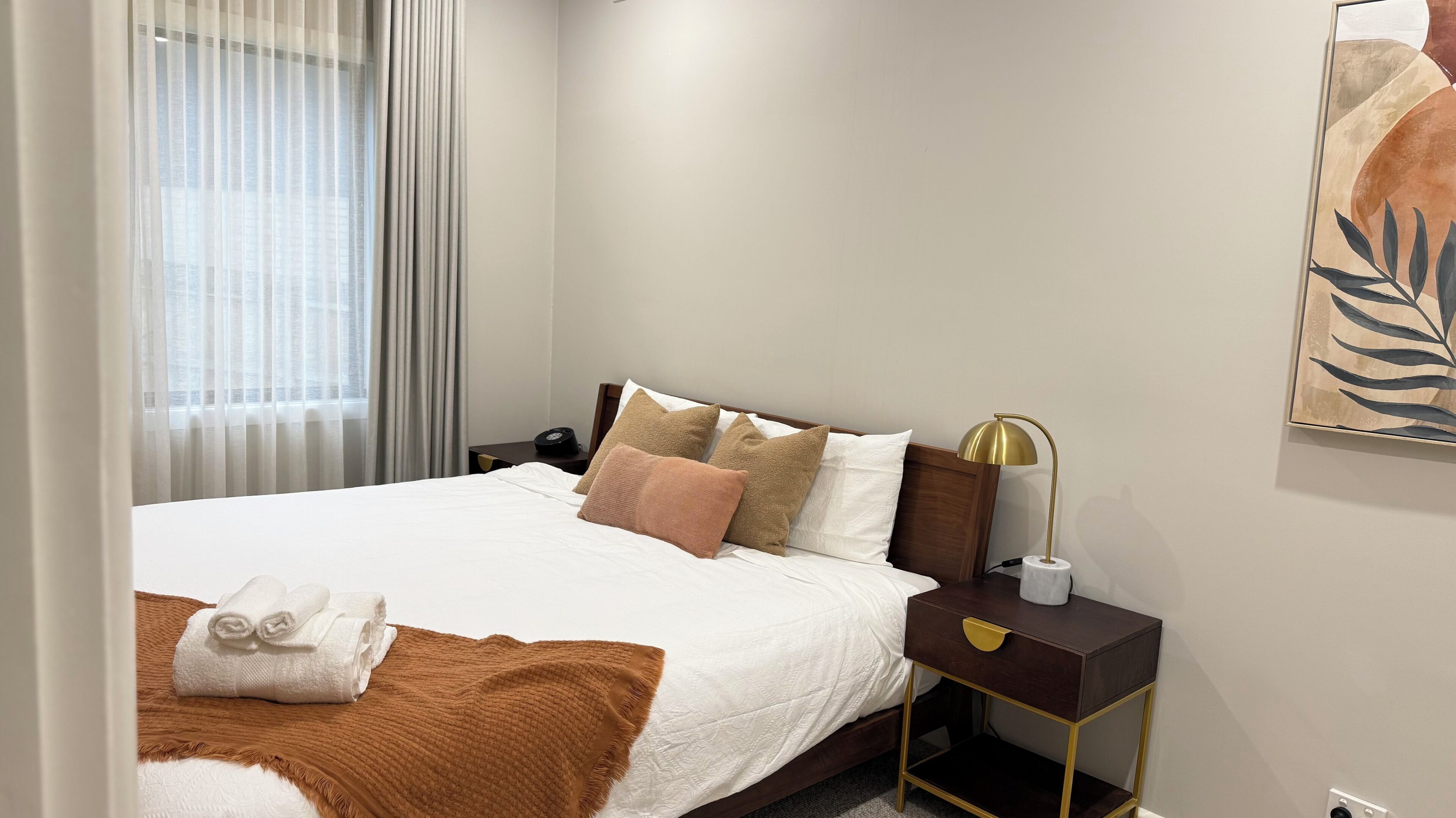 Ein Hotelzimmer mit Bett, Nachttisch, Lampe und einem Kunstwerk an der Wand.
