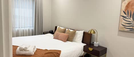 Ein Hotelzimmer mit Bett, Nachttisch, Lampe und einem Kunstwerk an der Wand.