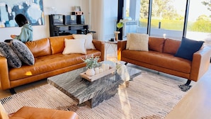 A modern living room with leather sofas, a coffee table, and a large window. - Peninsula Beach house (Mount Eliza)