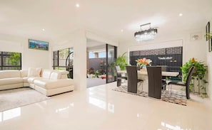 A modern living room with a white sofa, a dining table with chairs, and a chandelier. - Spacious 5BR Family Home| Fire Pit| Kids Area (Catherine Field)