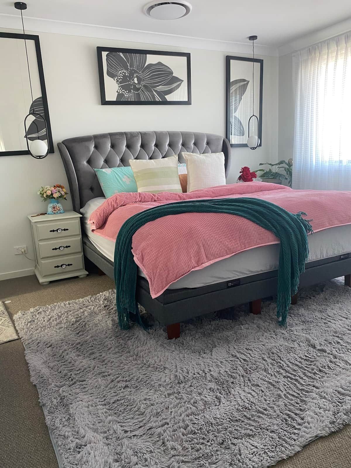 Un dormitorio con cabecera capitonada, cama con ropa de cama rosa y aguamarina, alfombra de pelo suave gris y decoración en la pared.