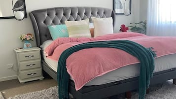 Un dormitorio con cabecera capitonada, cama con ropa de cama rosa y aguamarina, alfombra de pelo suave gris y decoración en la pared.