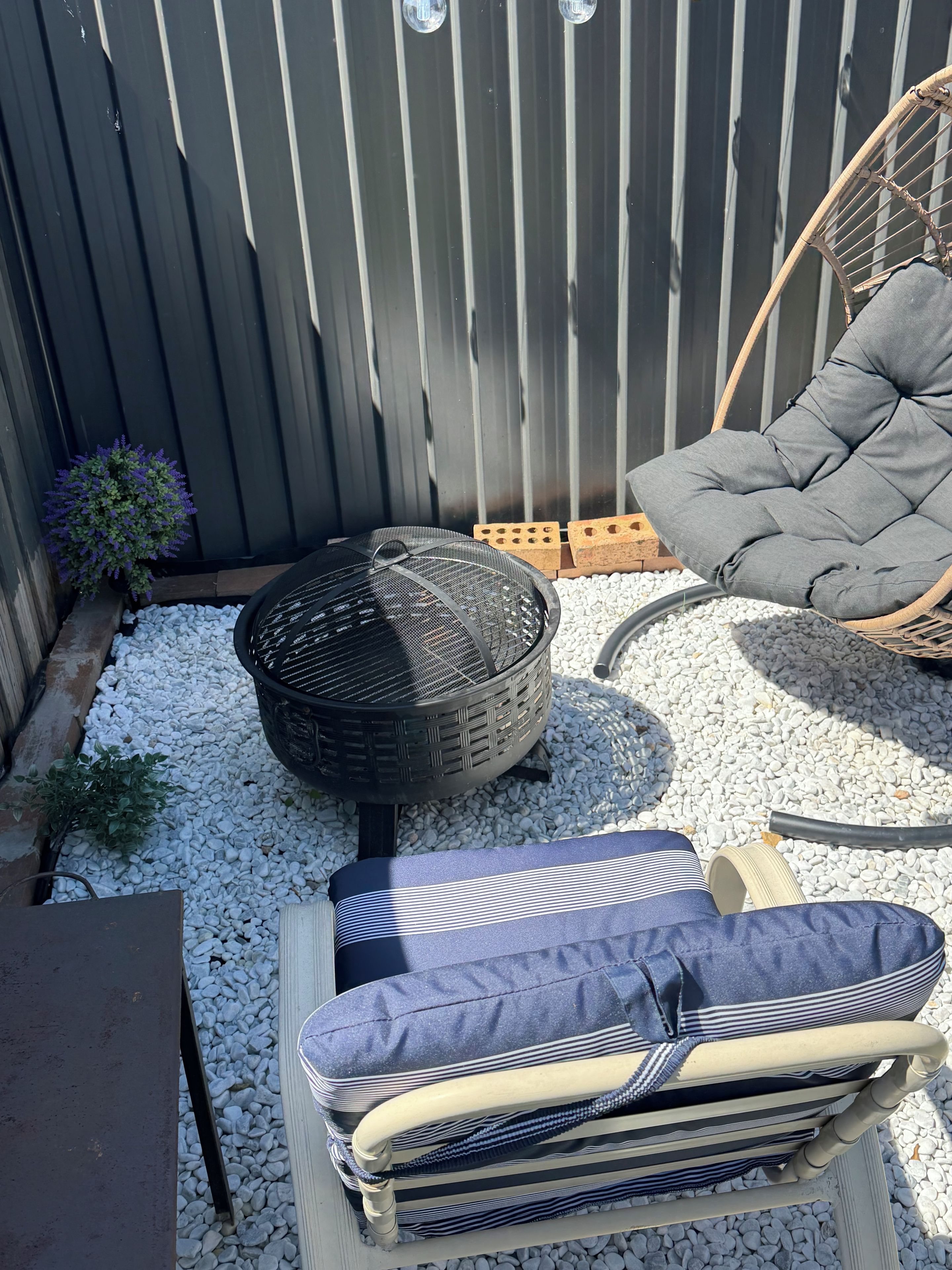 Eine Terrassenfläche mit einem Feuerkorb, einem gepolsterten Stuhl und einem gestreiften Kissen auf einem Tisch.