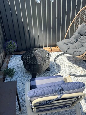 A patio area with a fire pit, a cushioned chair, and a striped cushion on a table.