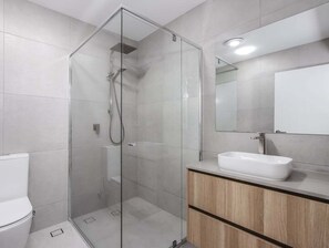 Ein modernes Badezimmer mit einer gläsernen Duschkabine, einem weißen Waschbecken und einem hölzernen Waschtisch.