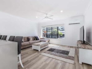 Ein modernes Wohnzimmer mit Sofa, Couchtisch, Fernseher und großen Fenstern.