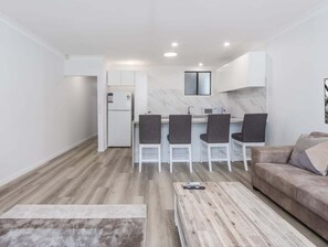 Eine moderne Küche mit weißen Schränken, einer Marmor-Spritzschutzwand und einem eingebauten Backofen. Vier dunkle Stühle stehen um die Kücheninsel.