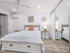 Um quarto com cama, mesas de cabeceira, ventilador de teto e decorações nas paredes.