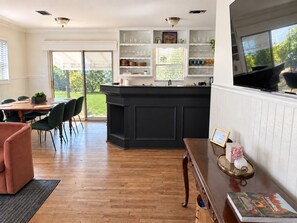 Eine moderne Küche mit einer schwarzen Kücheninsel, Essbereich mit Tisch und Stühlen sowie Ausblick ins Freie durch große Fenster.