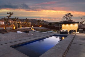 A pool area with a view of the mountains, outdoor seating, and a building with illuminated windows. - JT luxe Compound Pool, Spa, Floodlit Pickleball, Sauna, Dome (Joshua Tree)