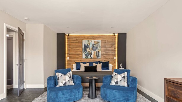 A modern hotel room with a bed, two blue armchairs, a small table, and a wooden accent wall with abstract art. - JT luxe Compound Pool, Spa, Floodlit Pickleball, Sauna, Dome (Joshua Tree)