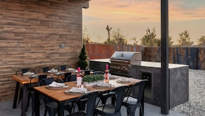 An outdoor dining area with a wooden table set for six, a grill, and a view of the sky. - JT luxe Compound Pool, Spa, Floodlit Pickleball, Sauna, Dome (Joshua Tree)