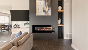 A modern living room with a fireplace, a dining area, and a large abstract painting. - JT luxe Compound Pool, Spa, Floodlit Pickleball, Sauna, Dome (Joshua Tree)