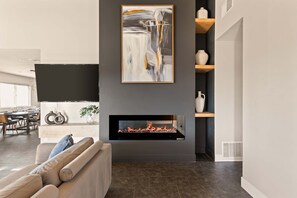 A modern living room with a fireplace, a dining area, and a large abstract painting. - JT luxe Compound Pool, Spa, Floodlit Pickleball, Sauna, Dome (Joshua Tree)