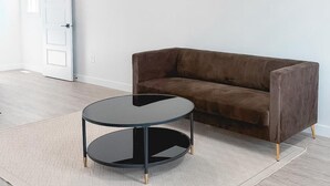 A room with a brown sofa, a round black table, and a patterned rug on a light wooden floor. - Serene 1-bedroom apartment in Edmonton (Edmonton)