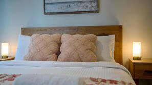 Ein Bett mit Holz-Kopfteil, zwei Zierkissen, einer weißen Bettdecke und zwei Nachttischlampen.